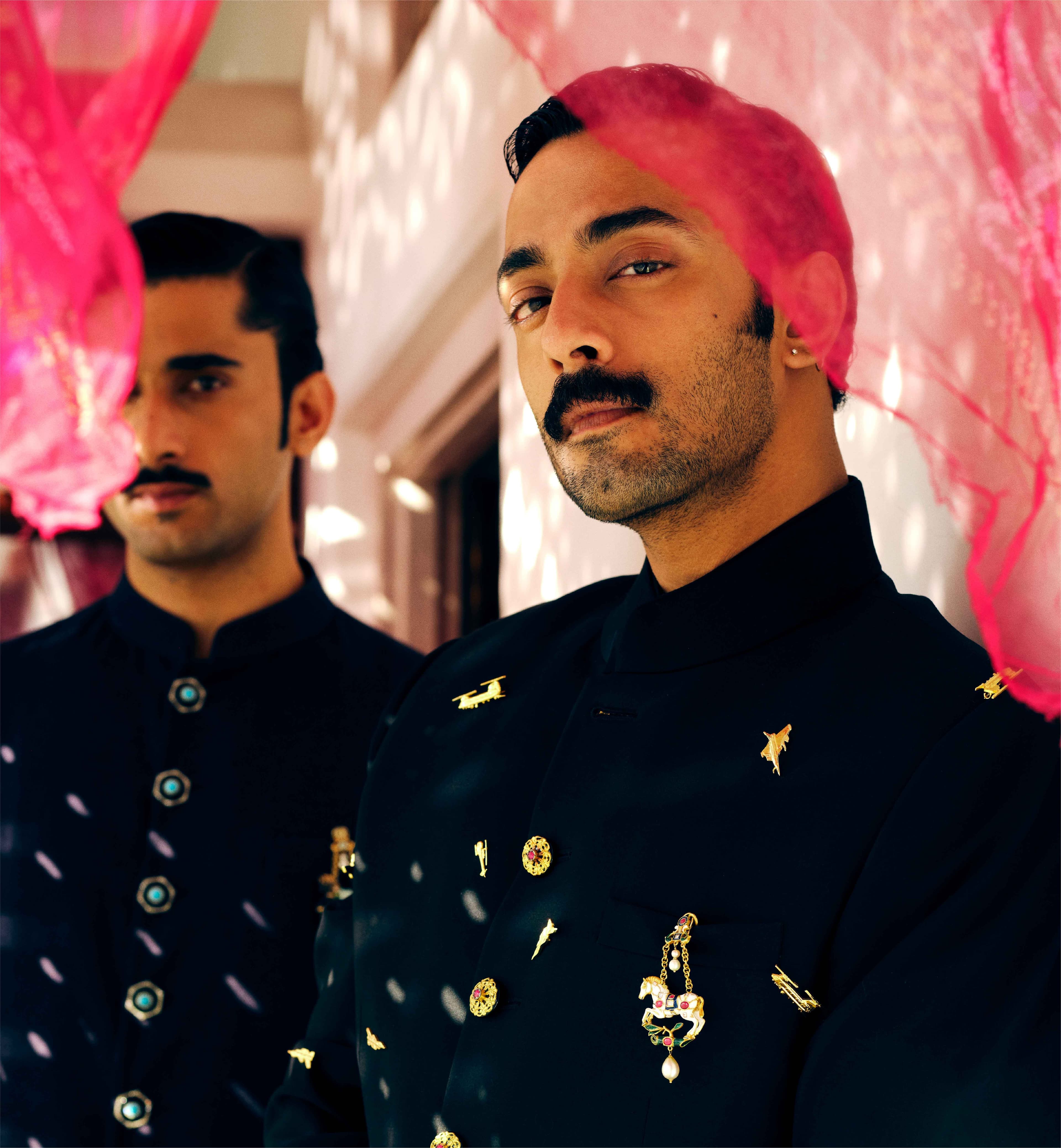 Mhaaro — two men in dark sherwanis, pink curtain backdrop