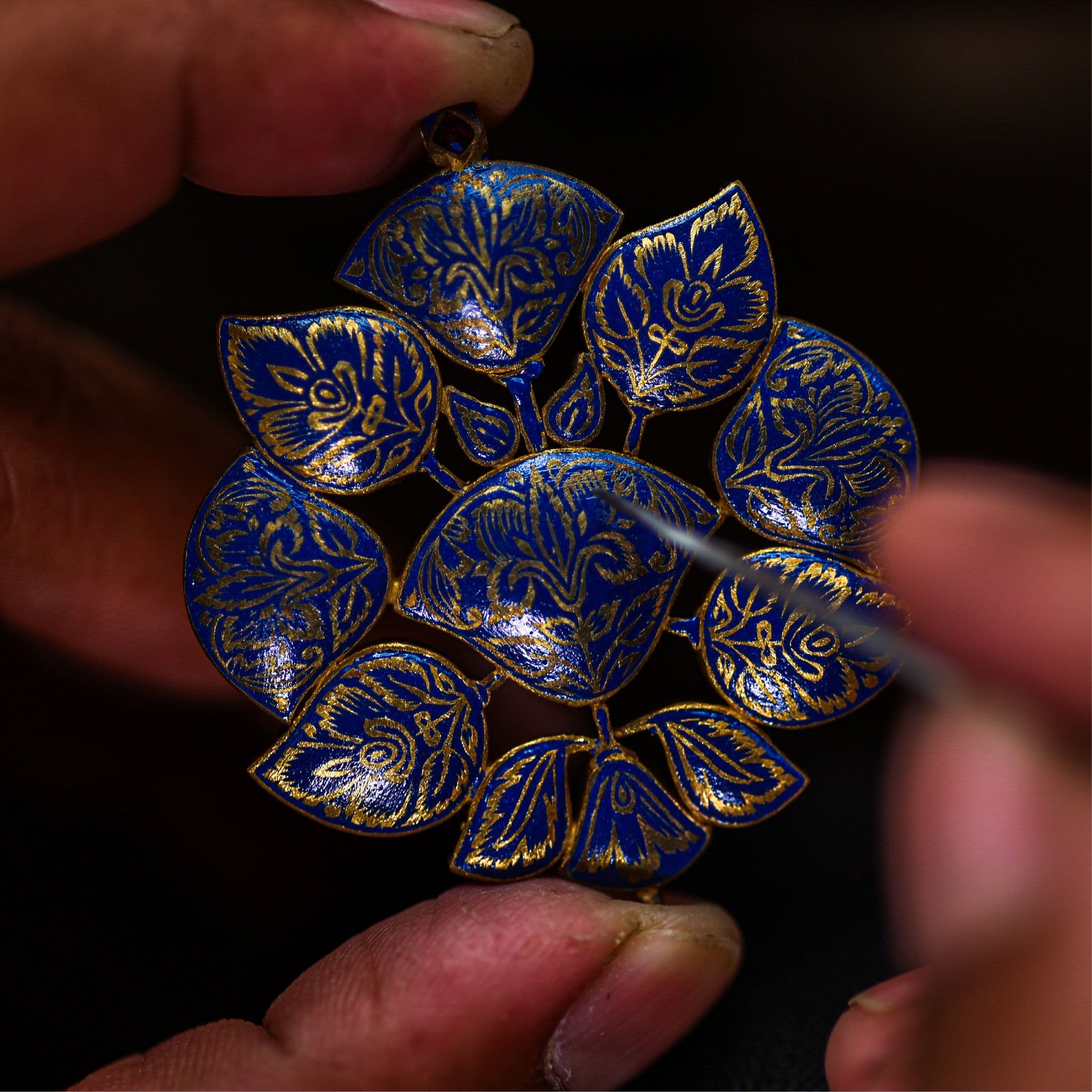Blue and gold meenakari pendant held between a karigar's fingers